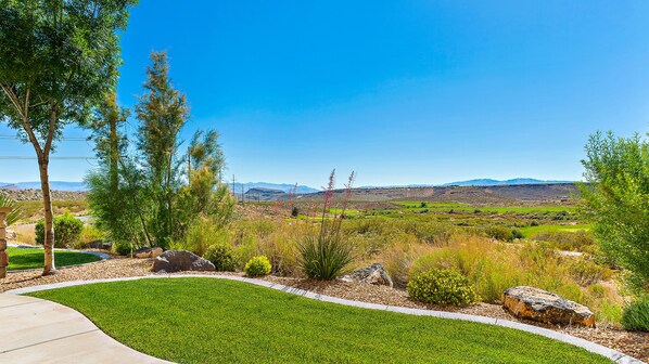 A landscaped garden with a curved pathway, various shrubs, and a view of distant mountains.