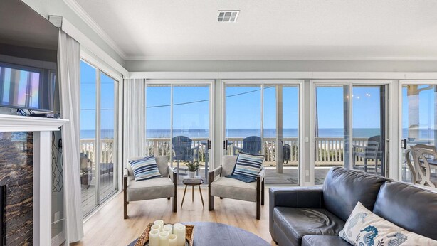 Ein geräumiger Wohnbereich mit großem Fenster zum Meer, ausgestattet mit einer Couch, Sesseln und einem Couchtisch.