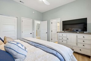 Un dormitorio con cama, televisor sobre una cómoda y un pasillo que conduce a otras habitaciones.