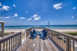 A wooden deck with chairs overlooking a beach.