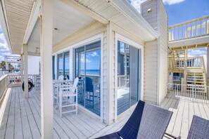 A covered outdoor deck with a glass enclosure, white furniture, and a view of the ocean.