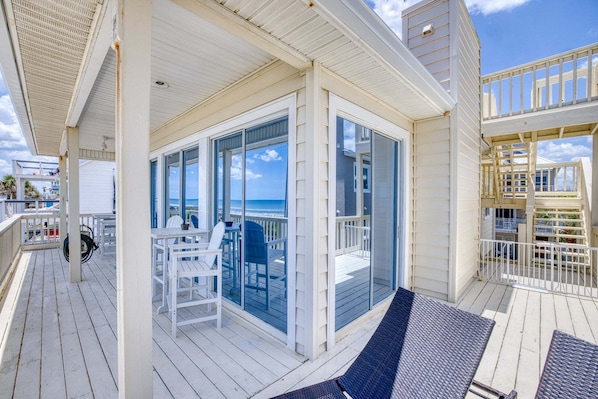 Une terrasse extérieure couverte, dotée d’une paroi vitrée, de mobilier blanc et offrant une vue sur l’océan.