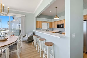 Una cocina moderna con armarios de madera, microondas y un refrigerador de acero inoxidable. Hay un comedor con una mesa redonda y taburetes de bar.