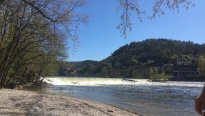 A river with a dam, surrounded by trees and a hill with buildings in the background. - House open on the countryside  (Albas)