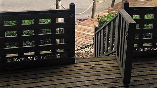 Una terraza de madera con vistas a un lago y árboles al fondo.