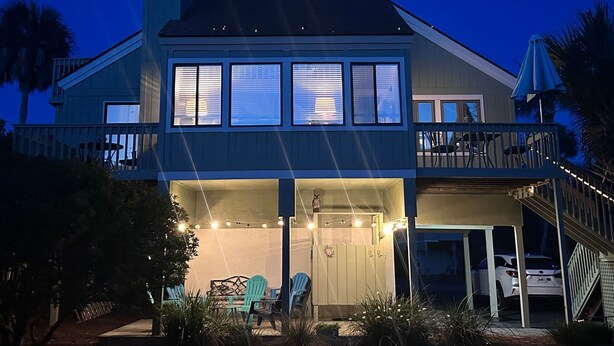 Ein zweistöckiges Haus mit Balkon, einer überdachten Terrasse und Sitzgelegenheit sowie einem Auto auf der Einfahrt.
