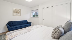 Een slaapkamer met een bed, een blauwe bank, een witte deur en een raam met uitzicht.