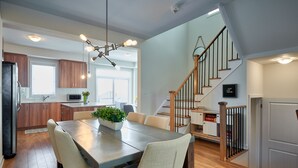 Une cuisine moderne avec des meubles en bois, un coin repas comprenant une table et des chaises, et un escalier menant à l’étage supérieur.