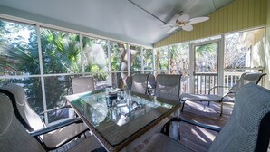 A sunlit room with a glass table and chairs, large windows, and a ceiling fan. - Beachy Cottage! Short Ride to Beaches, Pools, Dining, Golf! Pet Friendly! Amenity access included (Seabrook Island)