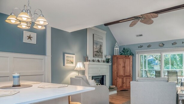 A kitchen with a central island, wooden bar stools, a ceiling fan, and a view of the outdoors through large windows. - Beachy Cottage! Short Ride to Beaches, Pools, Dining, Golf! Pet Friendly! Amenity access included (Seabrook Island)
