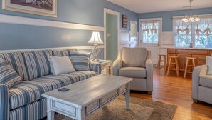 A living room with a striped sofa, a small table, a lamp, and a chair. There is a painting on the wall and a window with curtains. - Beachy Cottage! Short Ride to Beaches, Pools, Dining, Golf! Pet Friendly! Amenity access included (Seabrook Island)