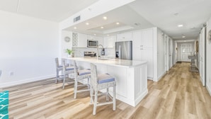 Una cocina moderna con muebles blancos, electrodomésticos de acero inoxidable y una isla central con taburetes de bar.