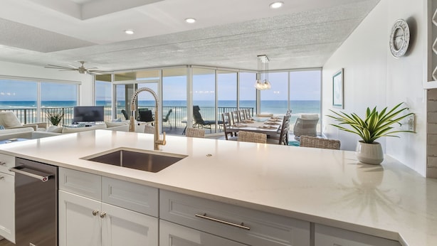 Una cocina moderna con una isla grande, muebles blancos y vistas al océano.