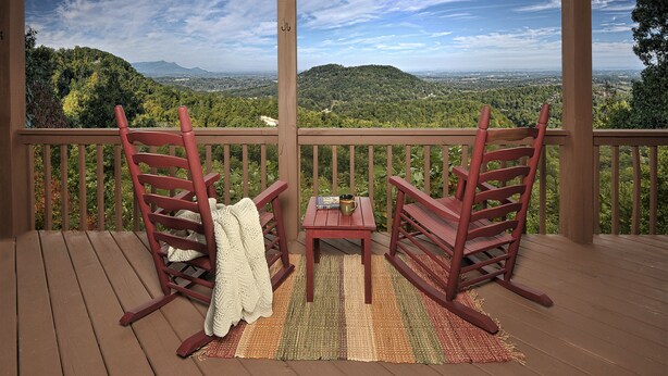 Eine Holzterrasse mit zwei Schaukelstühlen und einem kleinen Tisch, mit Blick auf eine malerische Landschaft mit Hügeln und Bäumen.