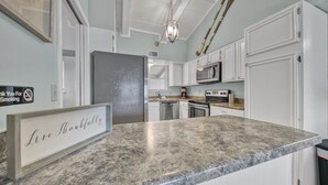 A kitchen with white cabinets, a granite countertop, stainless steel appliances, and a chandelier. - Beach Service Included, Private Beach, Chateau La Mer 10E! (Destin)