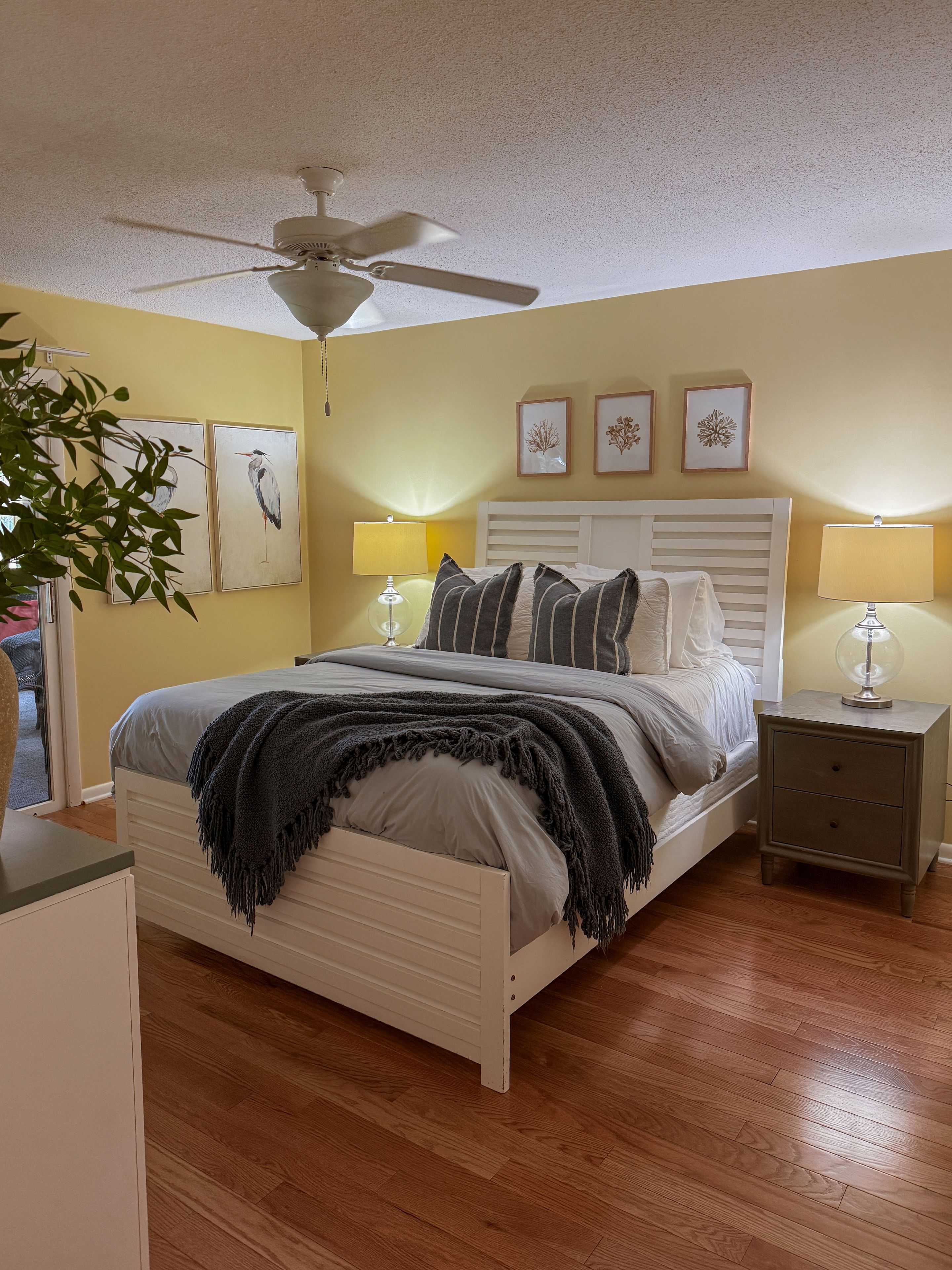 A bedroom with a bed, bedside tables, a ceiling fan, and wall art.