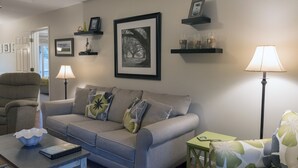 A living room with a grey sofa, a green armchair, a small table with a bowl and book, and two floor lamps. - Adorable Cottage! Pet Friendly! 3 BR/2 BA w/ Golf Views! Amenity access! (Seabrook Island)