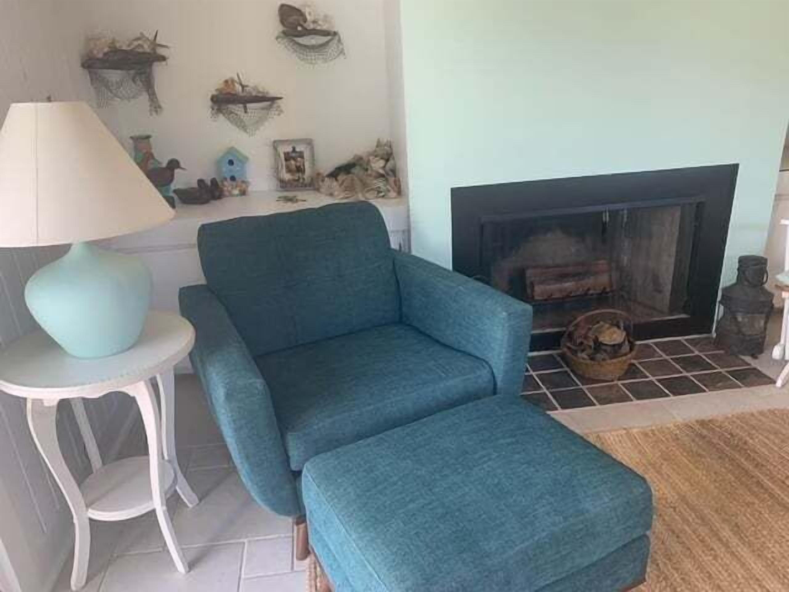 A living room with a teal armchair, a small side table with a lamp, a fireplace, and decorative wall art.