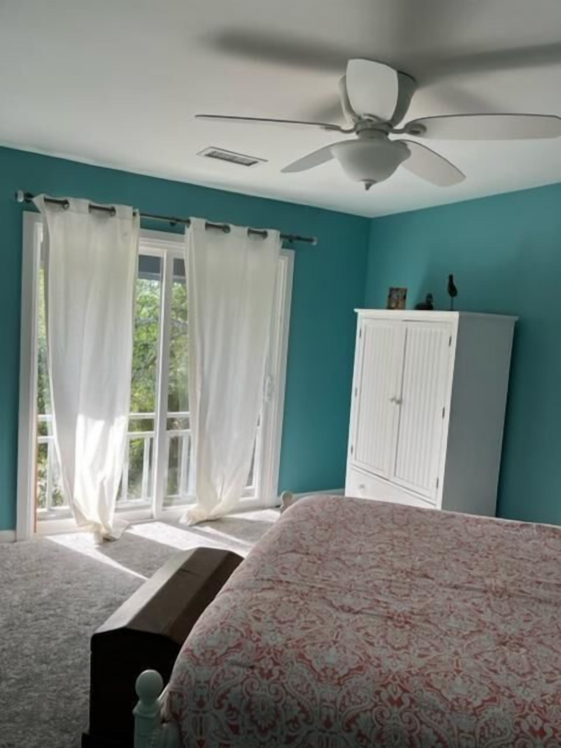 Une chambre à coucher avec un lit, un ventilateur de plafond, une armoire et une fenêtre avec des rideaux.