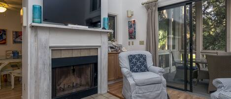 A living room with a fireplace, a television, and a dining area with a glass door leading outside.
