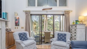 Un salón con dos sillones a rayas, un sofá azul, una mesa de centro con un control remoto y vistas al exterior a través de un ventanal.