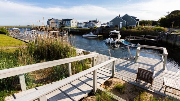 A wooden dock with benches, a small boat, and houses in the background. - "Sea Gypsy"  Waterfront newly renovated, beautiful views, dock, beach! (Dennis)
