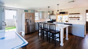A modern kitchen with a central island, stainless steel appliances, and a dining area with a white table and chairs. - "Sea Gypsy"  Waterfront newly renovated, beautiful views, dock, beach! (Dennis)