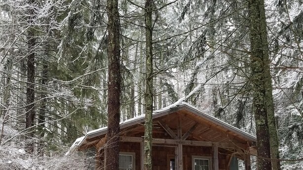 Una baita con portico in legno e scale che conducono ad essa, circondata da alberi innevati.
