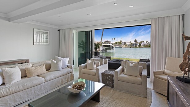 Una sala de estar moderna con un gran ventanal con vistas a una masa de agua, amueblada con sofás y una mesa de centro.