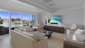 Un salón espacioso con un gran ventanal con vistas a un puerto deportivo, un televisor de pantalla plana montado en la pared y una zona de estar cómoda con sofás y una mesa de centro.