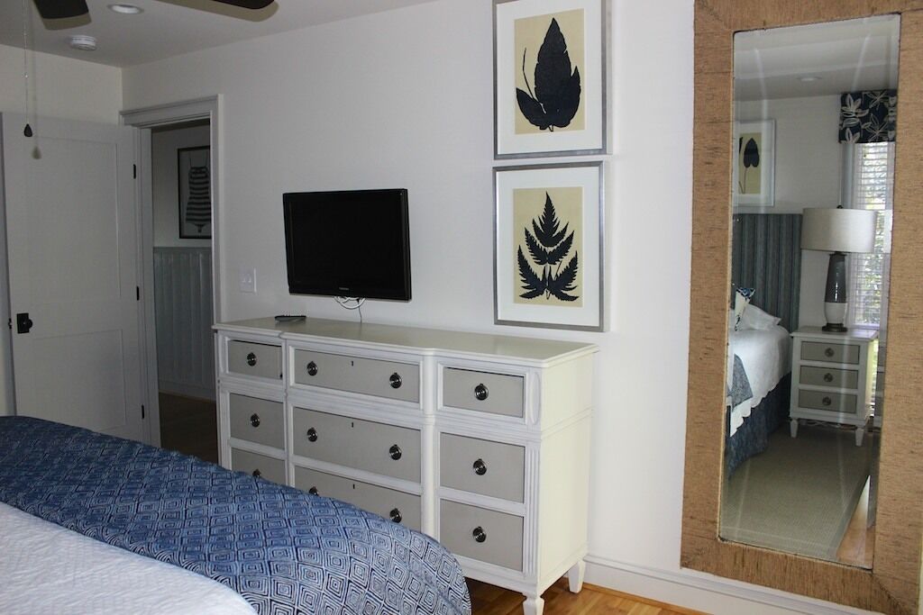 Een slaapkamer met een bed, een dressoir, een flatscreen televisie en bladkunst in een lijst aan de muur.