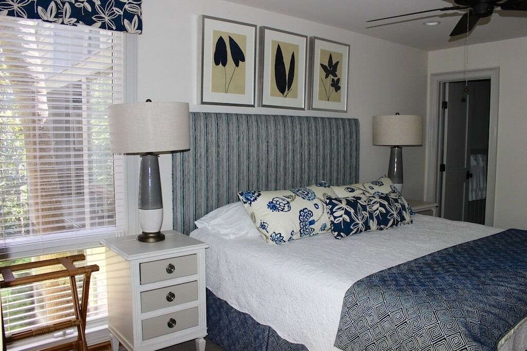 A bedroom with a bed, two bedside lamps, a nightstand, and a window with blinds.