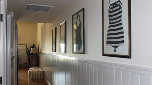 Un couloir orné de tableaux encadrés, avec une lampe et un pouf à rayures.