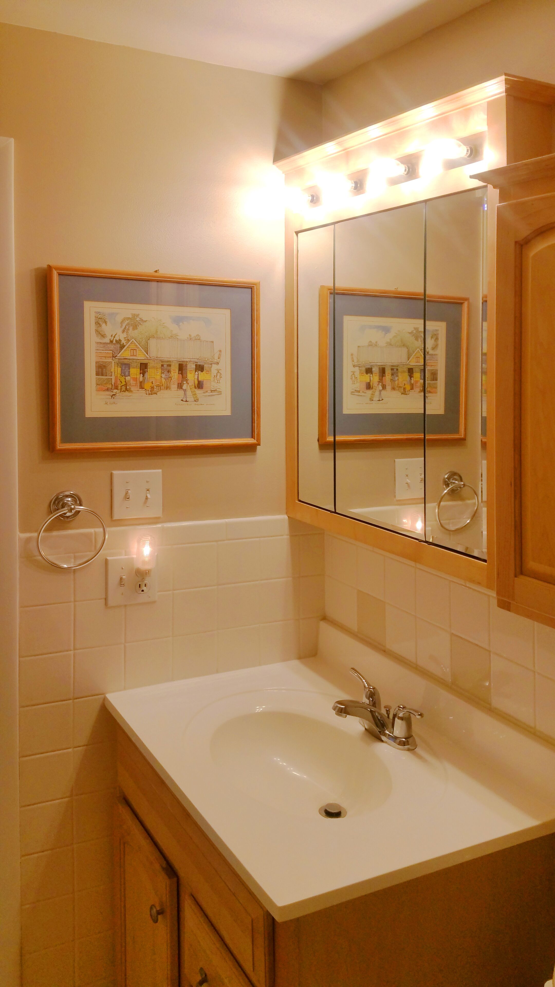 A bathroom with a white sink, a large mirror, and two framed pictures on the wall.