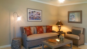A living room with a sofa, a coffee table, a floor lamp, and a lamp. There are two framed pictures on the wall. - 2 Bedroom 1,079 sf Cottage. Dock. Full Kitchen, WI-FI,HDTV, Parking & Pets ok. (Stuart)