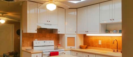 Una cocina con armarios blancos, estufa y ventilador de techo.