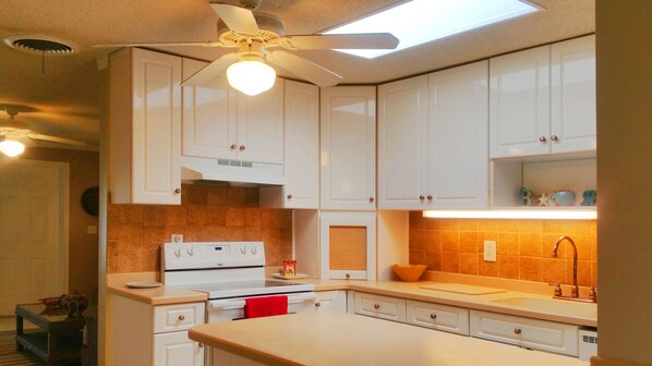 A kitchen with white cabinets, a stove, and a ceiling fan.