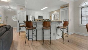 A modern kitchen with white cabinets, a central island with bar stools, and a microwave.
