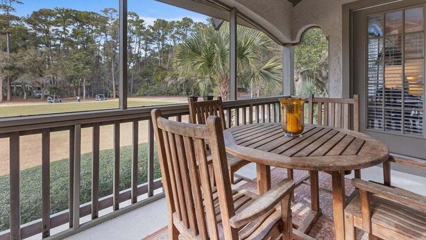A wooden deck with a round table and chairs, overlooking a baseball field.