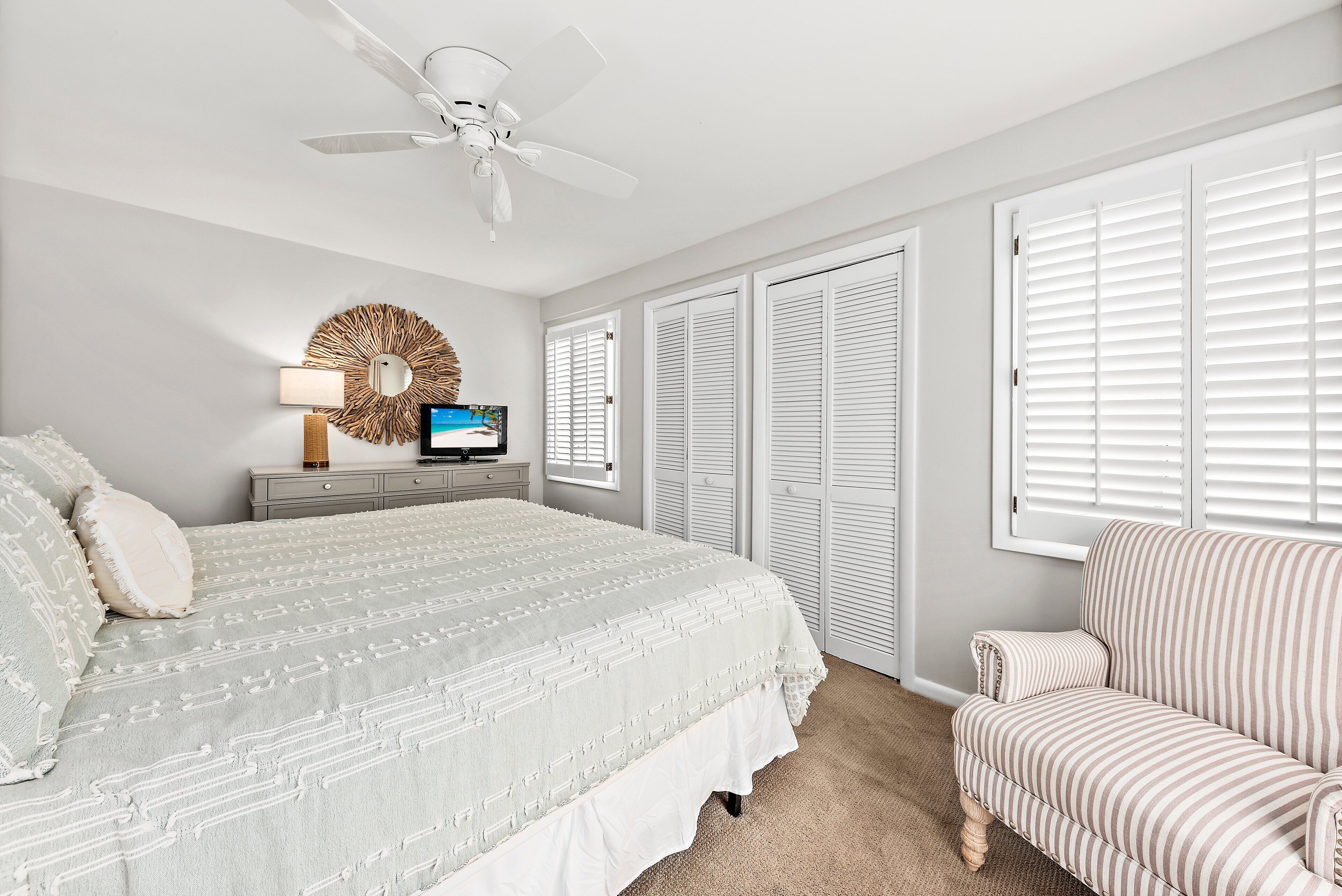 A bedroom with a bed, a chair, a TV, a ceiling fan, and a wardrobe.