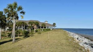 A beachfront property with a large house, palm trees, and a rocky shoreline.