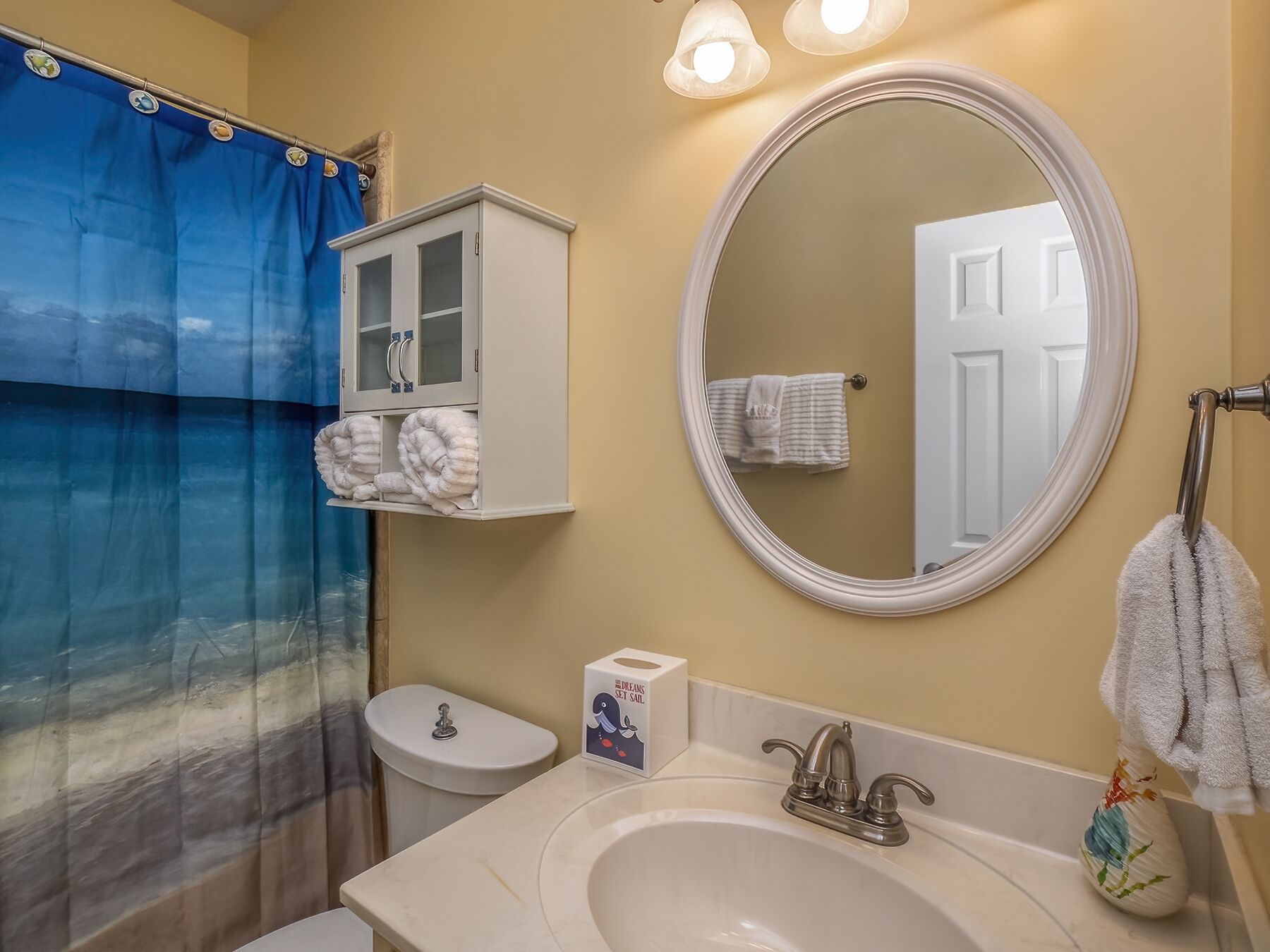 Un baño con lavamanos blanco, un espejo, un inodoro y un mueble con toallas.
