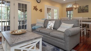 A cozy living room with a grey sofa, a wooden coffee table, and a dining area with a white table and chairs.