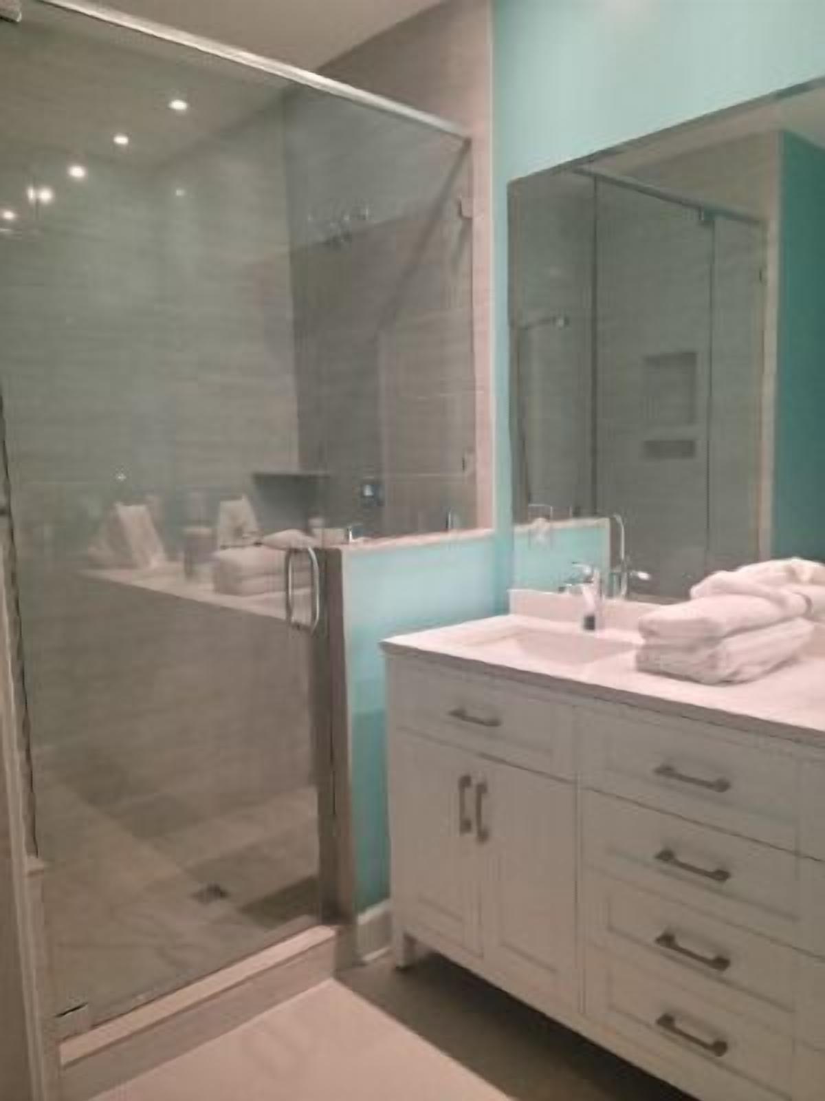 A modern bathroom with a glass shower enclosure, a large mirror, and a white vanity with multiple drawers.