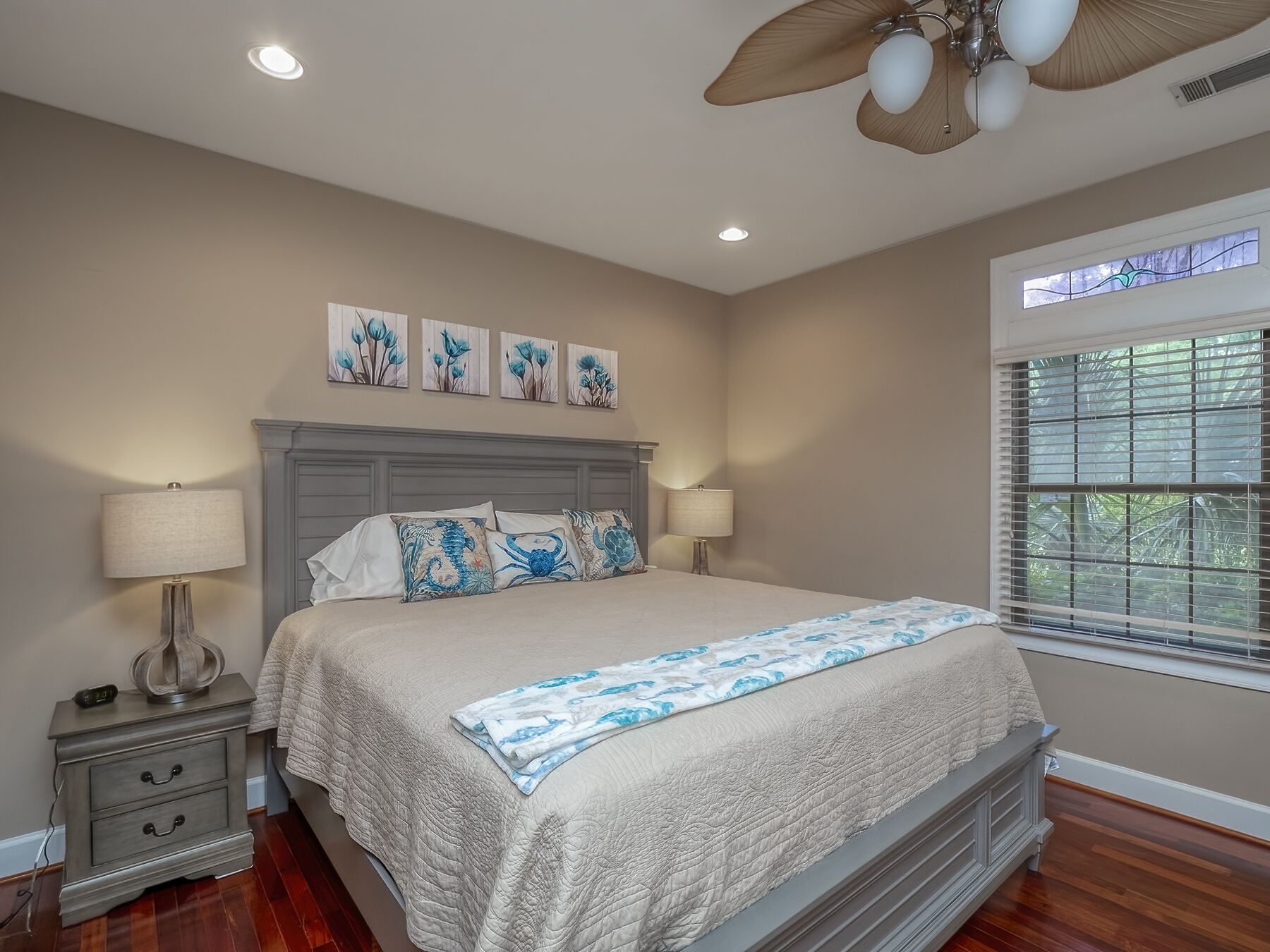 A bedroom with a bed, two bedside tables with lamps, a ceiling fan, and artwork on the wall.