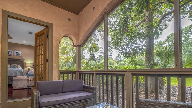 A cozy outdoor seating area with wicker furniture, a glass-top table, and a view of lush greenery.