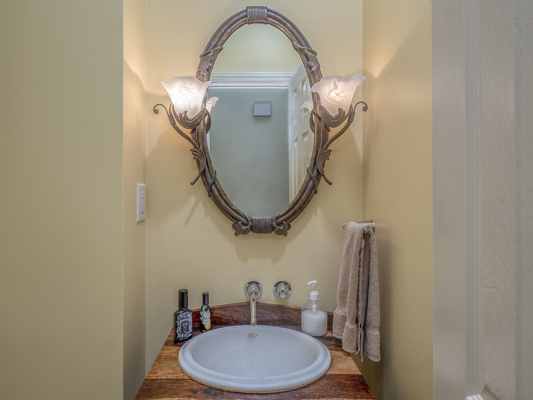 Une salle de bain avec un meuble-lavabo en bois, un lavabo blanc, un miroir avec un cadre décoratif et un porte-serviettes.