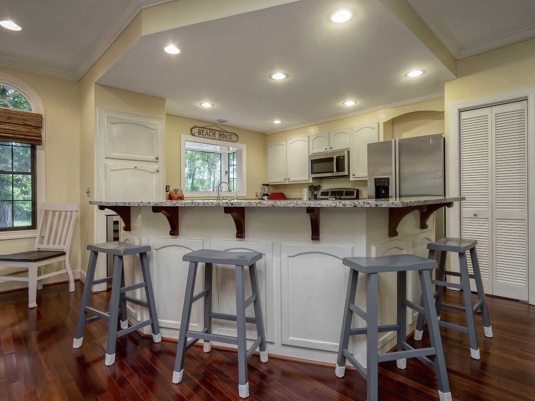 A kitchen with a central island, white cabinets, a stainless steel refrigerator, and a sign reading "Beach House".