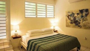 Een slaapkamer met een bed, twee bedlampen, een raam met zonwering en een wandairconditioner.