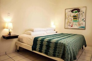 A bedroom with a bed, a bedside table with a lamp, and a wall-mounted painting. - R Casa Unit 2 at Steps Beach (Rincón)